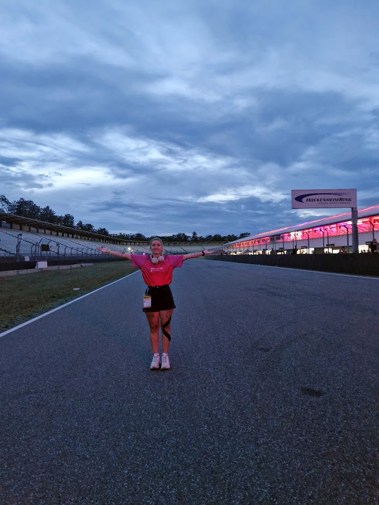 Dehlya on the start-finish straight at the Hockenheimring during a Formula Student event, arms outstretched at dusk.